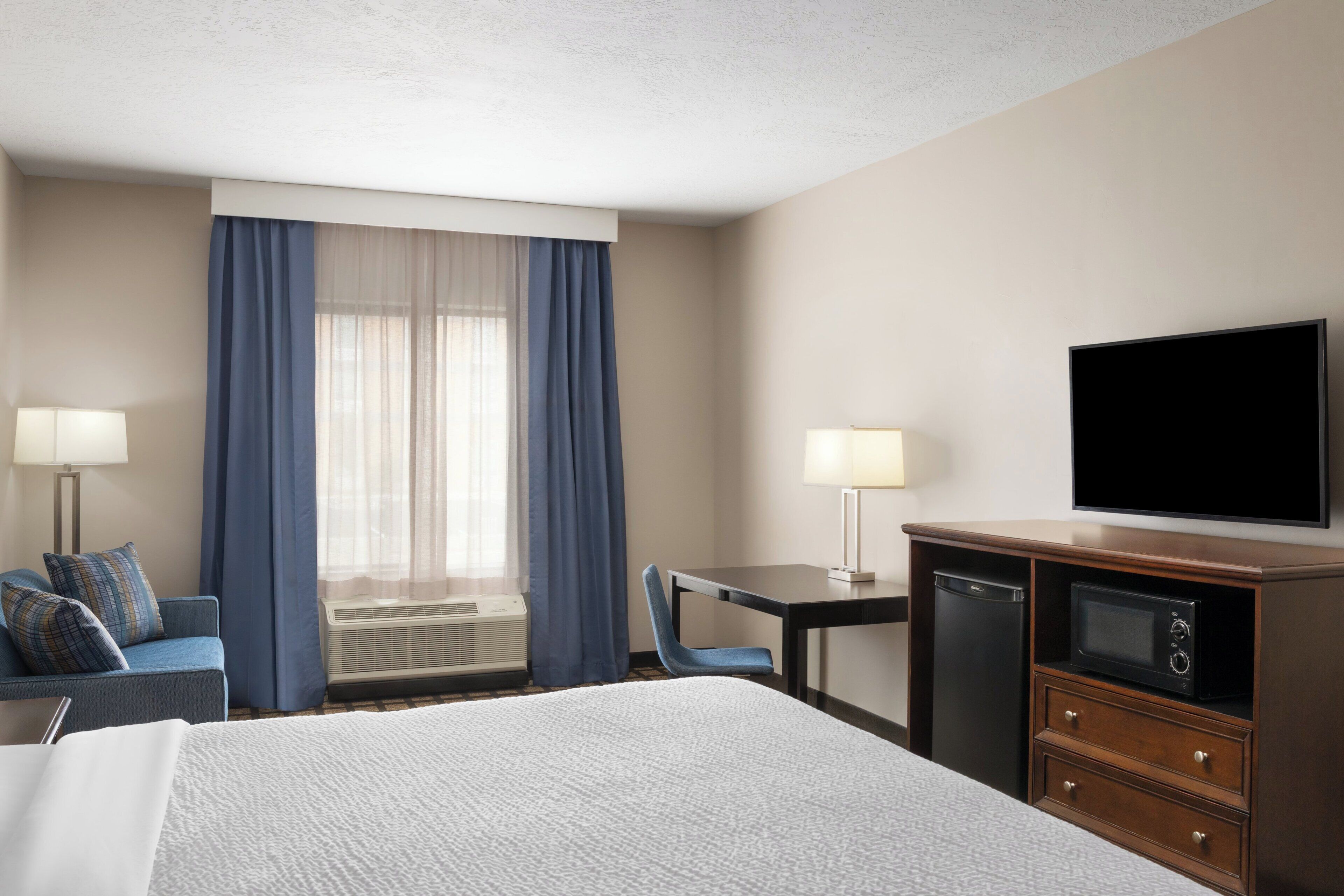 A hotel room with a bed, a desk, a television, and a window with curtains.