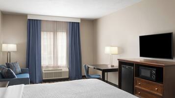 A hotel room with a bed, a desk, a television, and a window with curtains.
