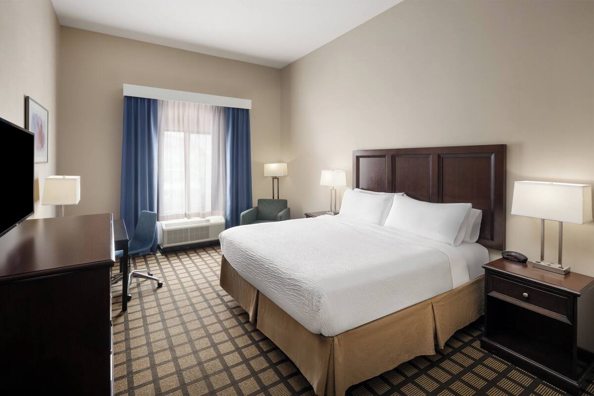 Une chambre d’hôtel avec un grand lit, deux tables de chevet avec des lampes, un bureau avec une chaise et une fenêtre avec des rideaux.
