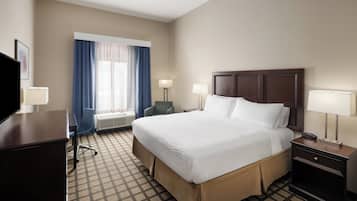 Een hotelkamer met een groot bed, twee nachtkastjes met lampen, een bureau met stoel en een raam met gordijnen.