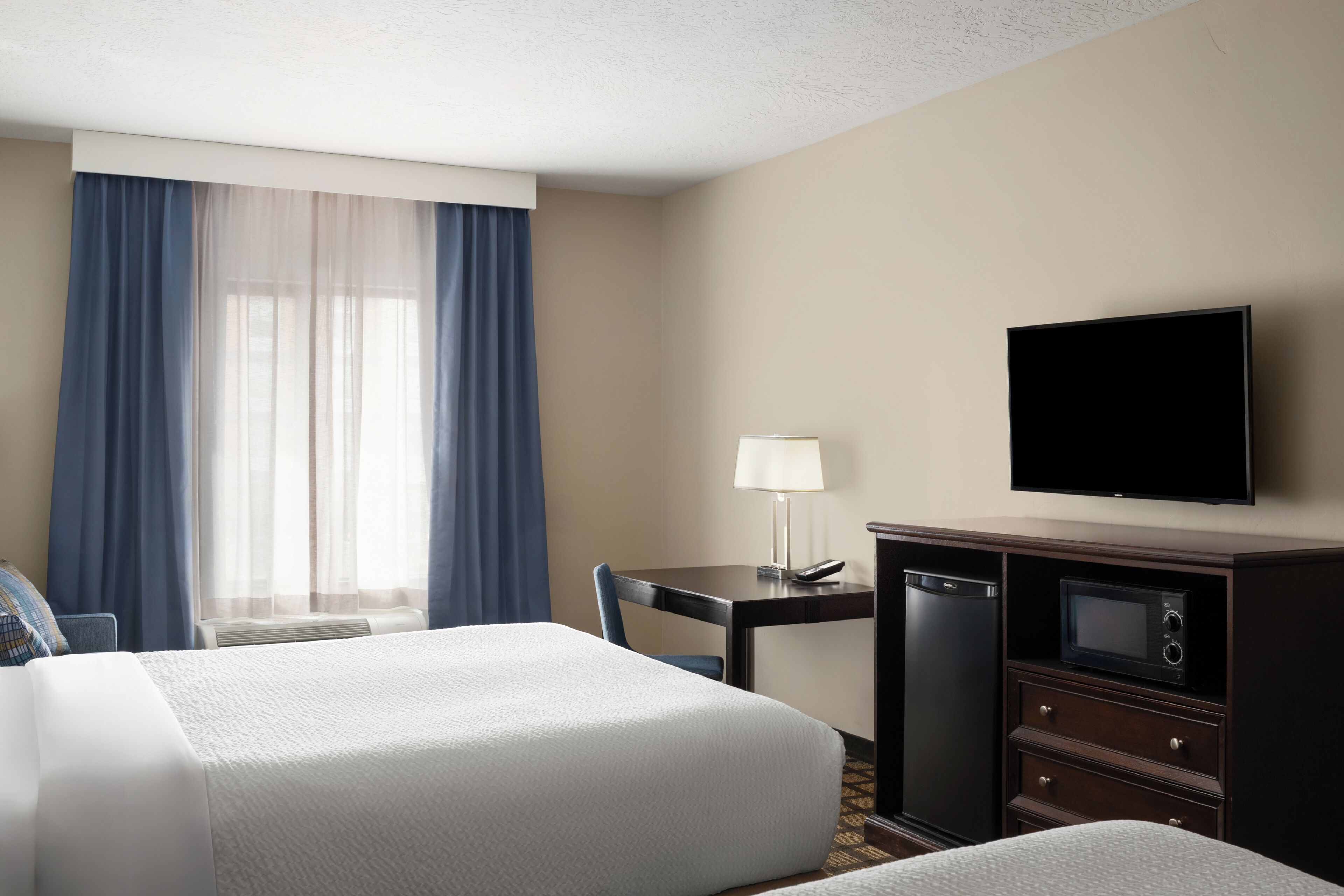 A hotel room with two beds, a desk with a lamp, a television, a microwave, and a refrigerator.