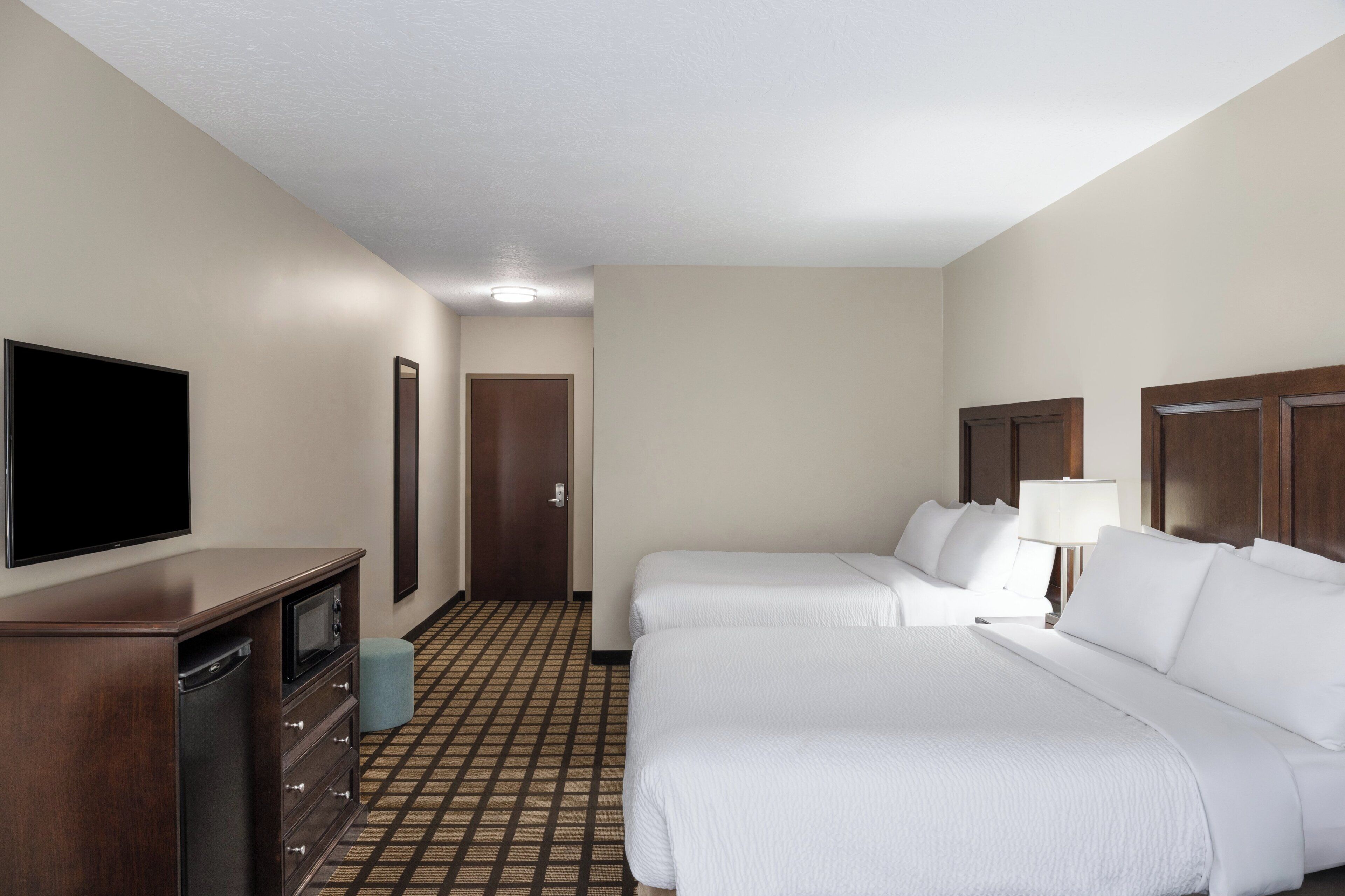 Une chambre d’hôtel avec deux lits, une télévision, une commode et une porte donnant sur une autre pièce.