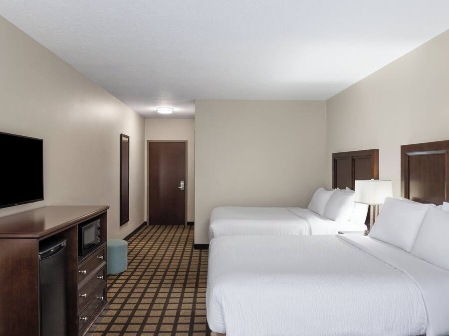 Une chambre d’hôtel avec deux lits, une télévision, une commode et une porte donnant sur une autre pièce.