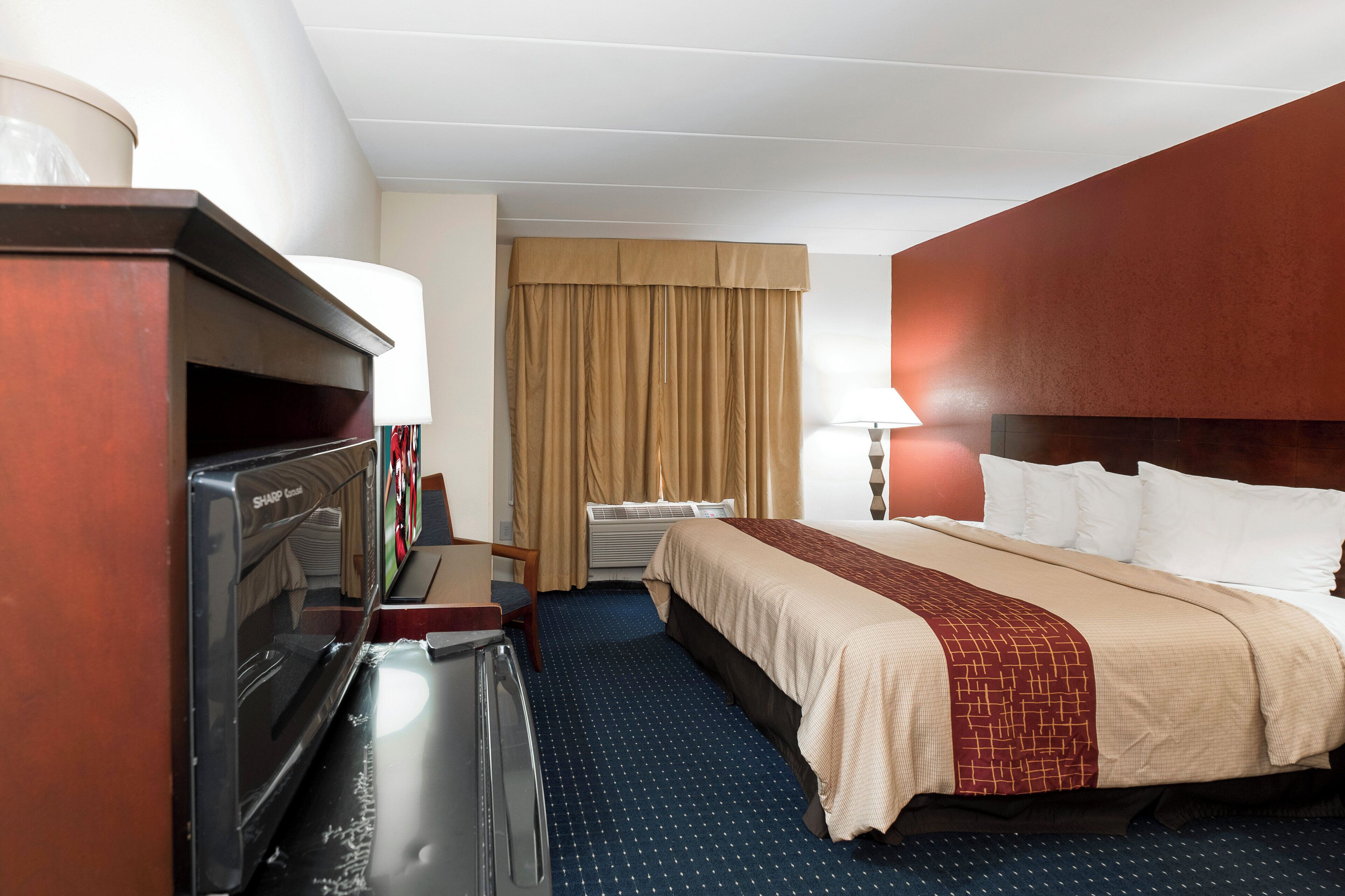 Une chambre d’hôtel avec un lit, un bureau, une télévision et une fenêtre avec des rideaux.