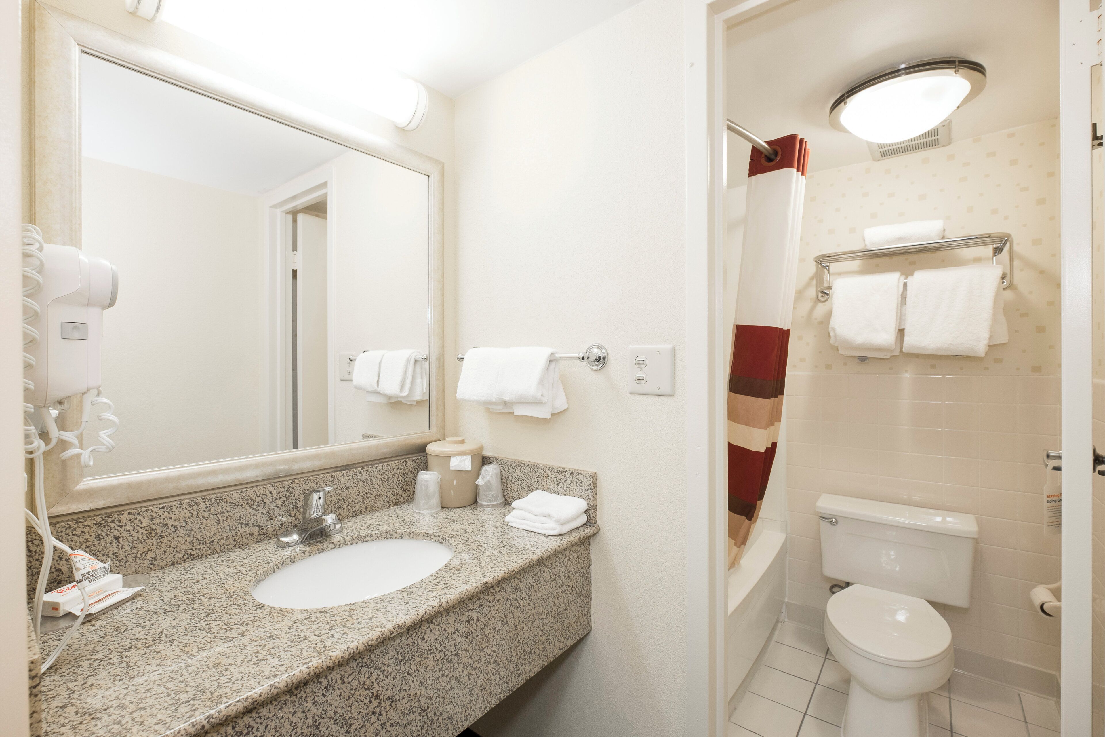 A bathroom with a granite countertop sink, a mirror, a towel rack, a toilet, and a shower area.