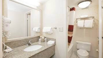 A bathroom with a granite countertop sink, a mirror, a towel rack, a toilet, and a shower area.