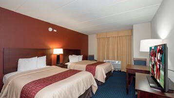 A hotel room with two beds, a desk, a television, and a window with curtains.