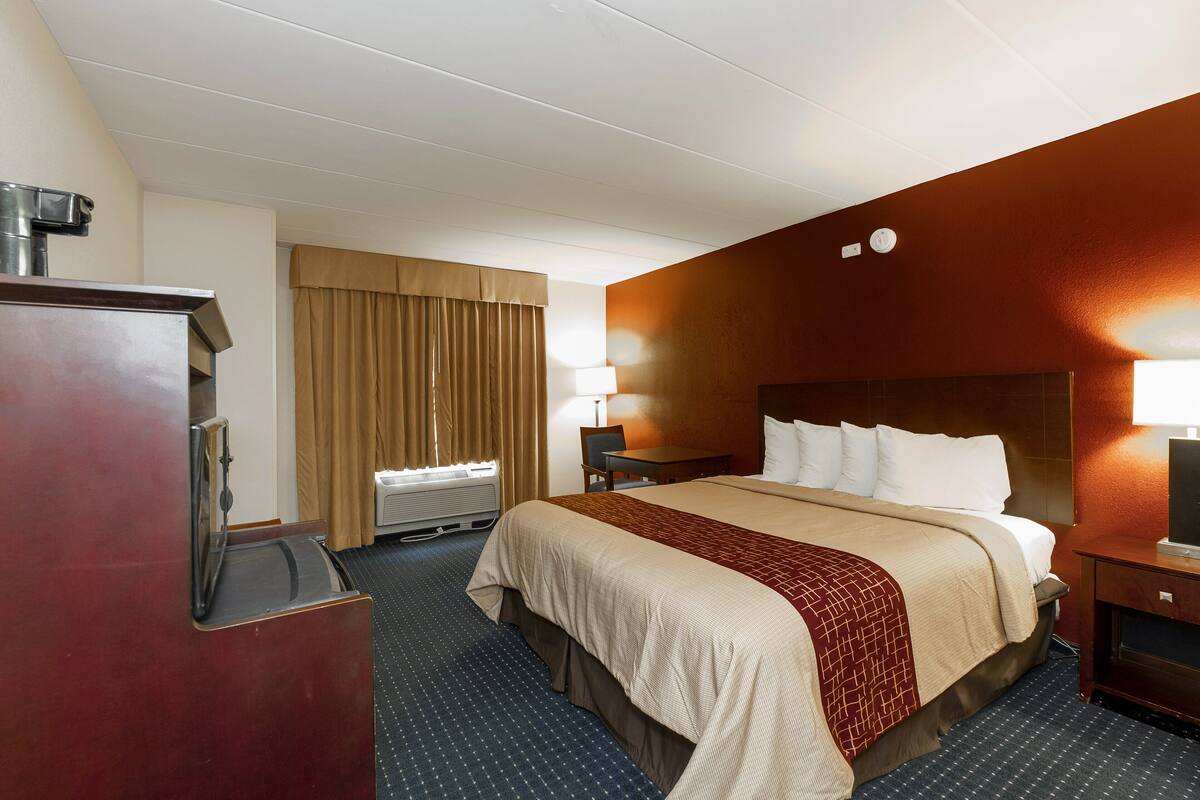 A hotel room with a large bed, a desk, a chair, a desk lamp, a TV, and a window with curtains.