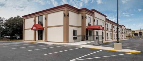 A hotel with a parking lot, two red awnings, and a clear sky.