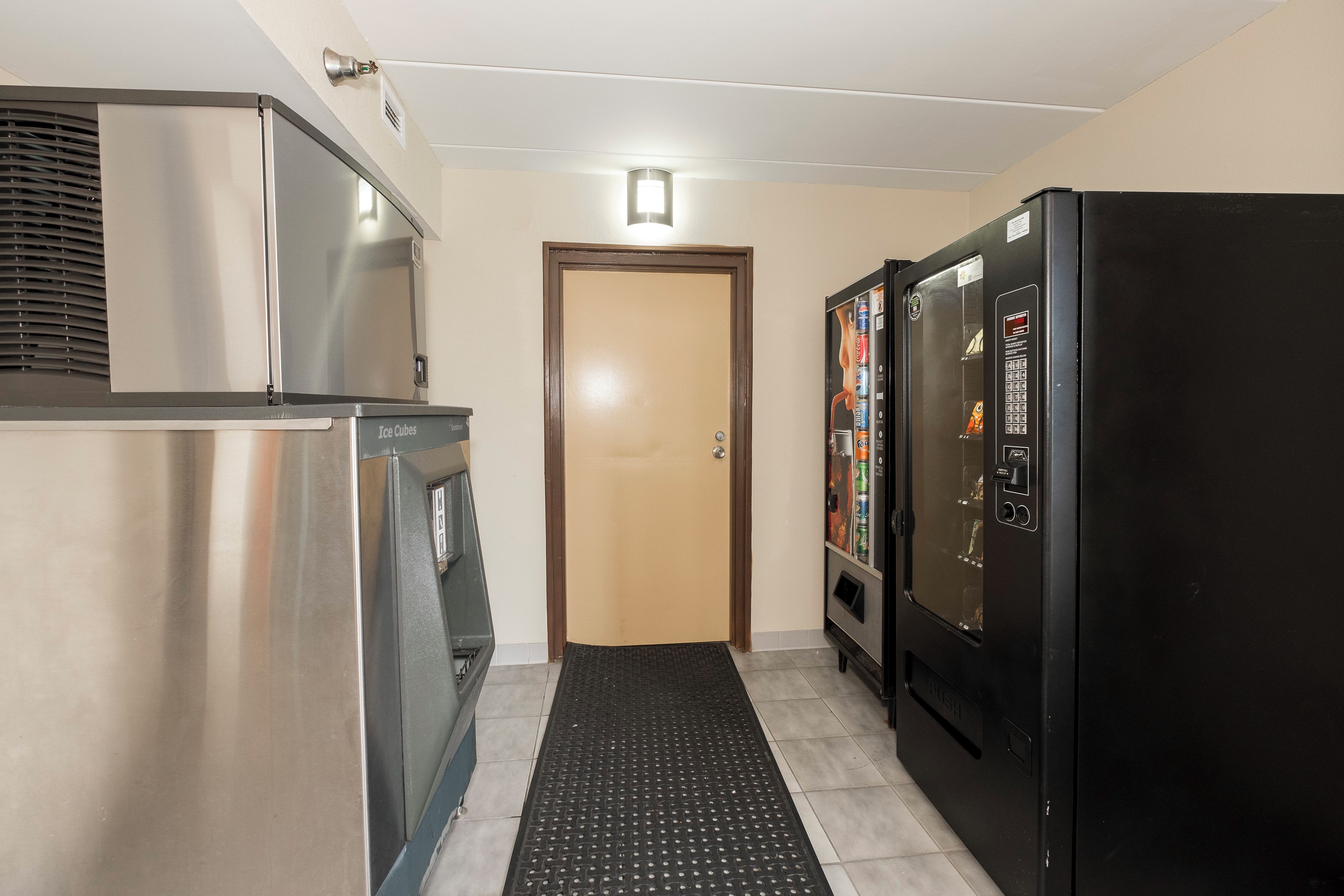 A hallway with a stainless steel refrigerator, a vending machine, and a door.