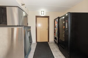 Un pasillo con un refrigerador de acero inoxidable, una máquina expendedora y una puerta.