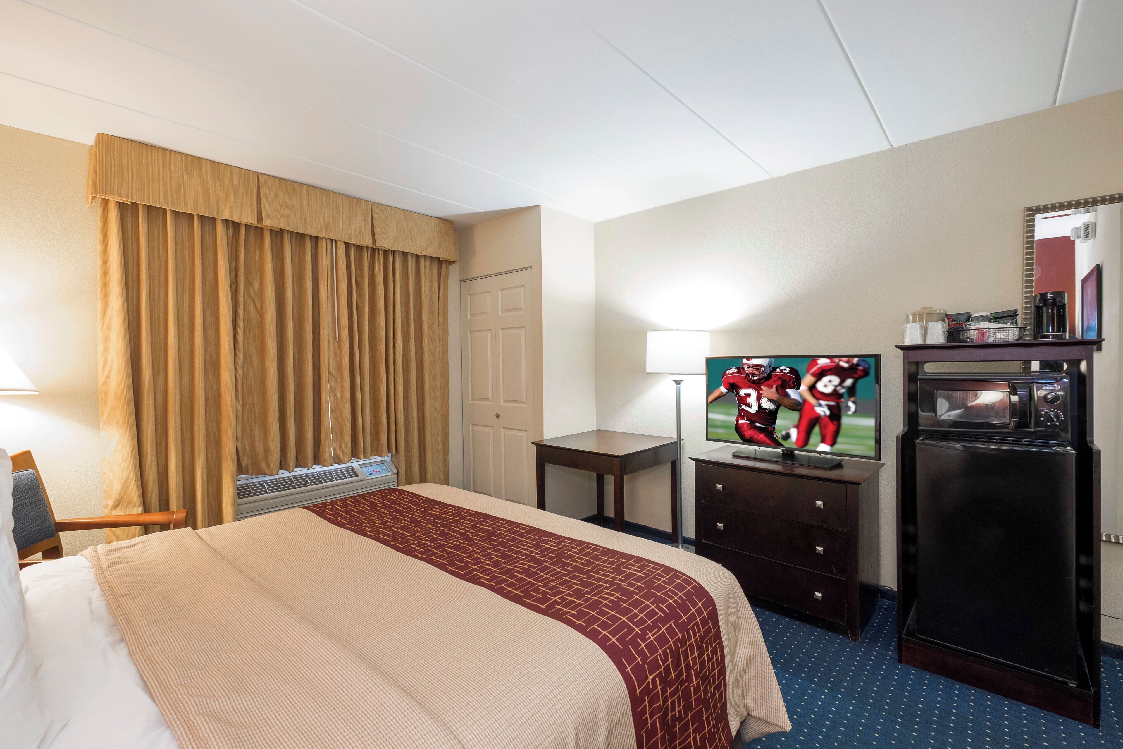 A hotel room with a bed, a television, a desk, and a refrigerator.