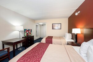 A hotel room with two beds, a desk, a chair, a TV, a mirror, and a door leading to another room.