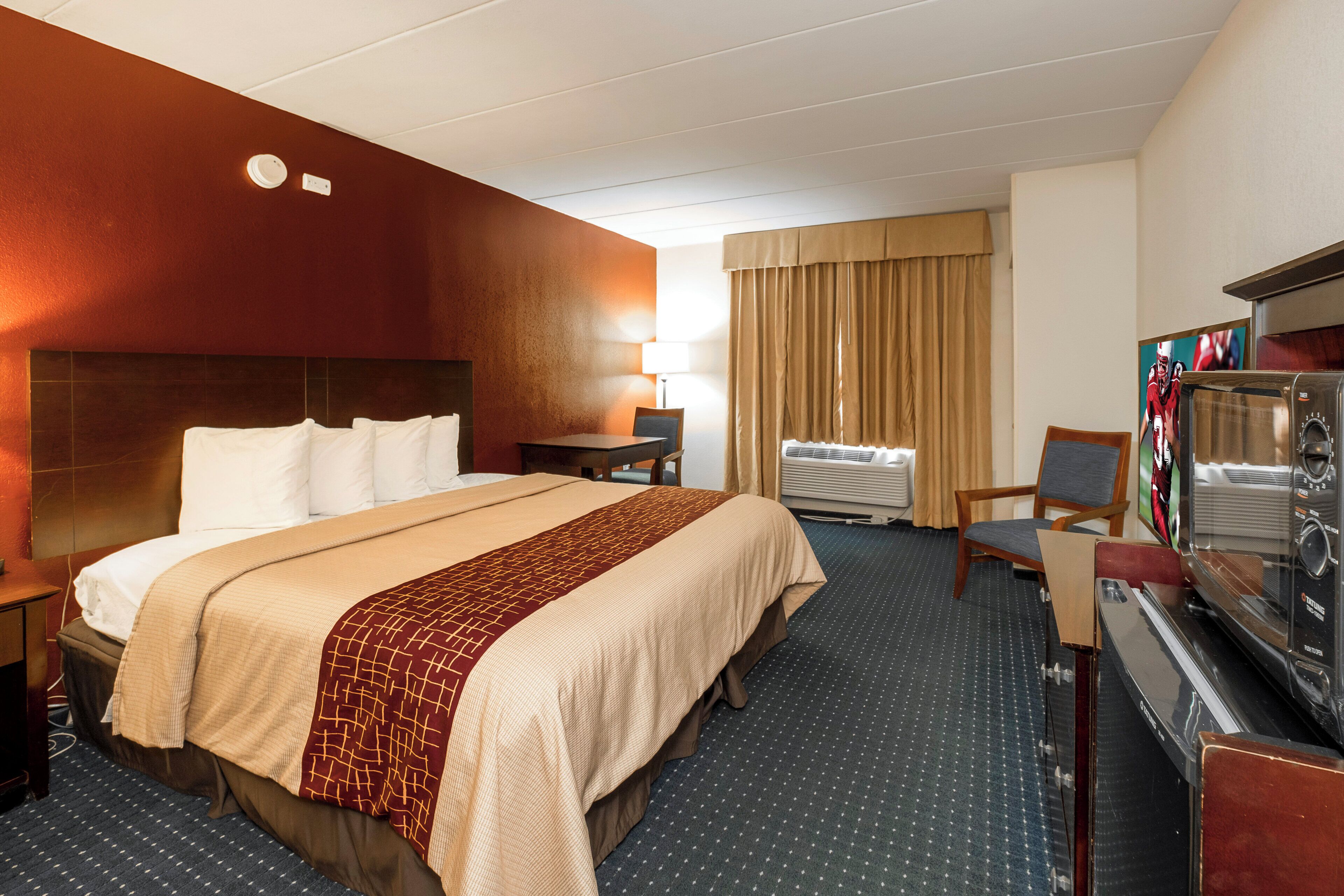 A hotel room with a bed, a desk with a television, a chair, and a window with curtains.