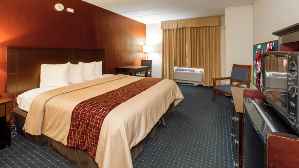 A hotel room with a bed, a desk with a television, a chair, and a window with curtains. - Red Roof Inn Annapolis (Annapolis)