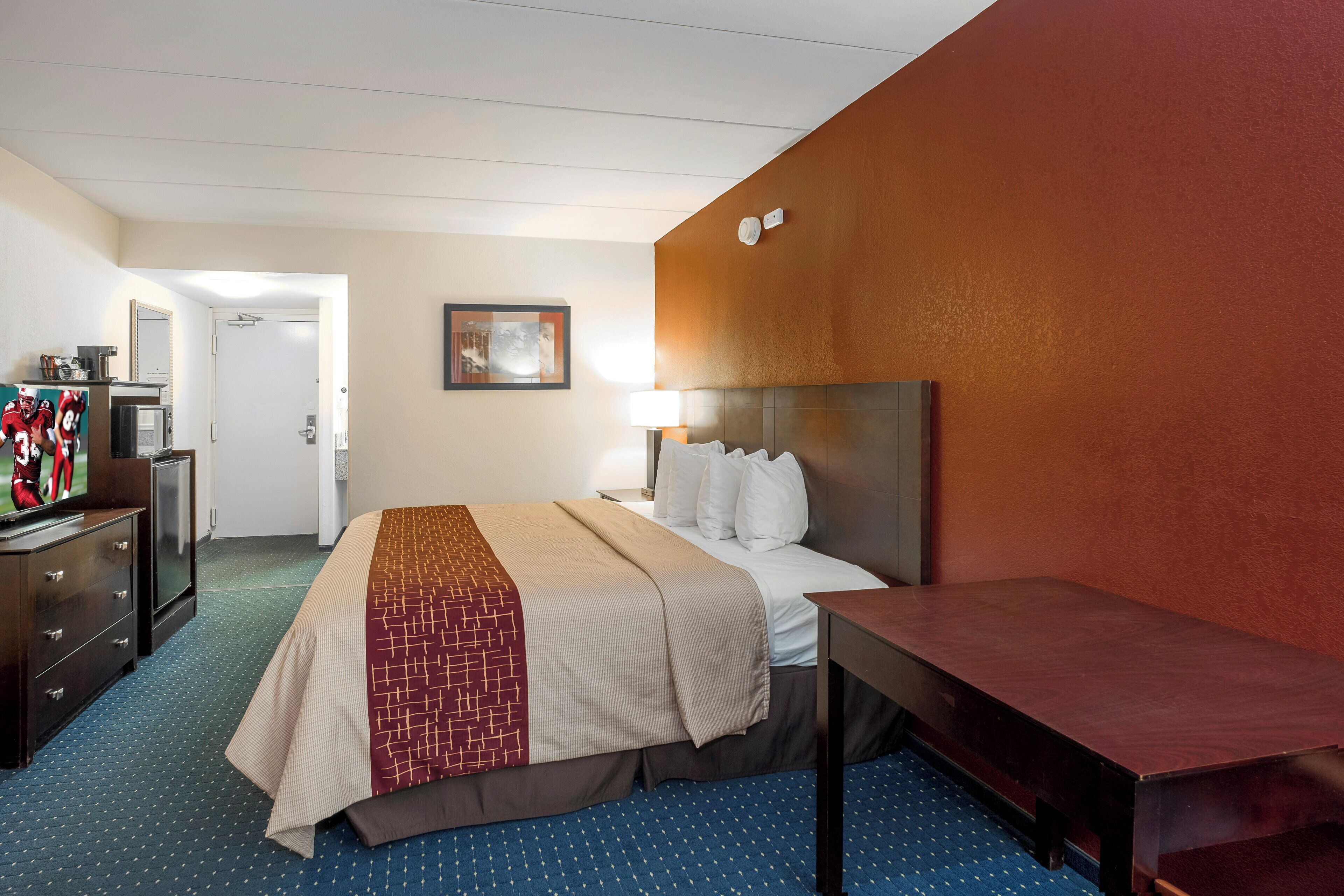 A hotel room with a bed, a desk, a dresser, and a television.
