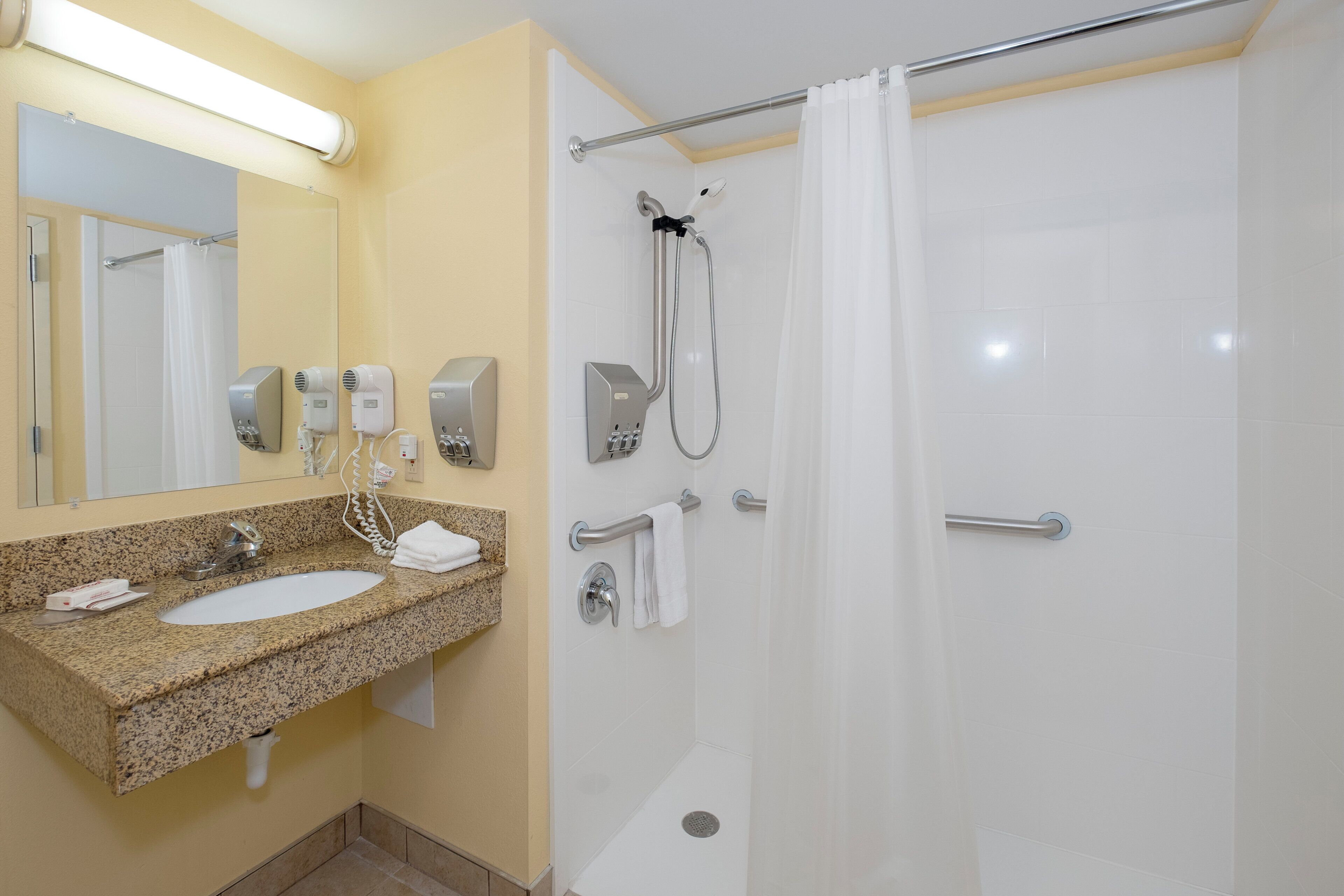Ein Badezimmer mit einem Waschbecken aus Granit, einem Spiegel, einem Handtuchhalter, einer Dusche mit Duschbrause und einer Glastür.