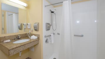 Ein Badezimmer mit einem Waschbecken aus Granit, einem Spiegel, einem Handtuchhalter, einer Dusche mit Duschbrause und einer Glastür.