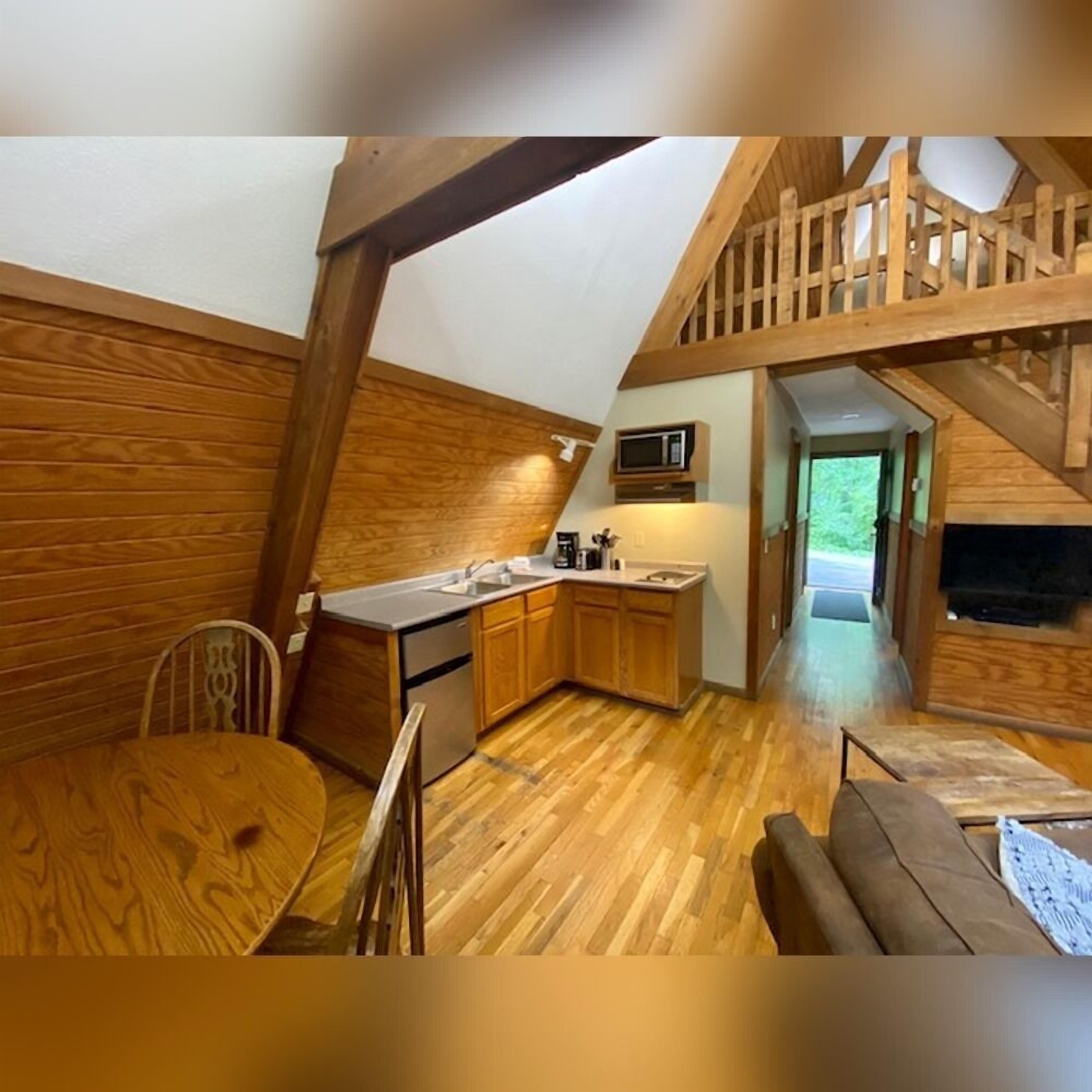 Une cuisine compacte avec des meubles en bois, une table à manger et un escalier menant à une mezzanine.