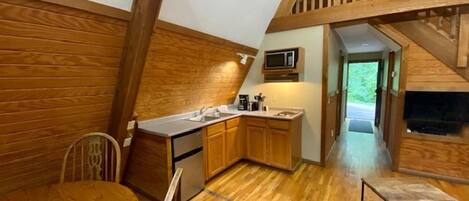 Une cuisine compacte avec des meubles en bois, une table à manger et un escalier menant à une mezzanine.