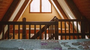 An attic room with a sloped ceiling, wooden beams, and a window. - A-Frame #17 - Hosted by The Chalets (Logan)