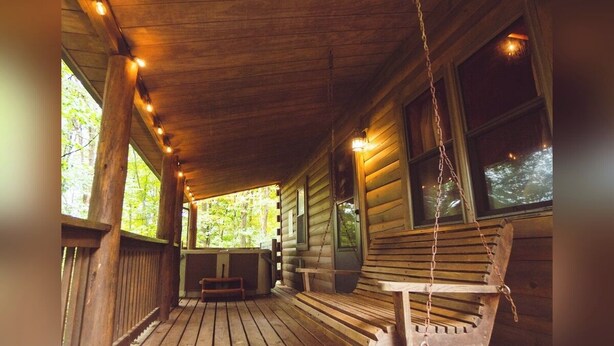 Une véranda en bois avec une balançoire, des rampes en bois et des guirlandes lumineuses.