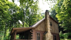 Une cabane en rondins avec une cheminée en pierre, une terrasse en bois et une antenne parabolique.