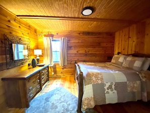 Ein Schlafzimmer einer Holzhütte mit einem Bett, einer Kommode, einem Spiegel und einem Fenster mit Vorhängen.