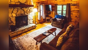 Un intérieur de chalet chaleureux avec une cheminée en pierre, des murs en bois, un téléviseur et un coin salon confortable.
