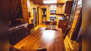 L’intérieur d’un chalet en bois comprend une table à manger, des chaises, un banc, un lustre et un coin cuisine.