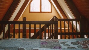 A room with a sloped ceiling, wooden beams, and a window. - A-Frame #18 - Hosted by The Chalets (Logan)