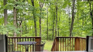 A hot tub with a wooden deck and a table and chair, surrounded by a forest. - A-Frame #18 - Hosted by The Chalets (Logan)