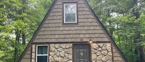 A small, triangular-shaped cabin with a stone facade, a single door, and a window on the upper floor.
