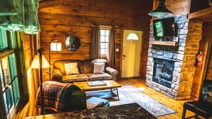 Interior acogedor de una cabaña con chimenea de piedra, paredes de madera, un sofá y un televisor.