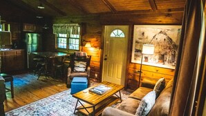 Un acogedor interior de cabaña con techo de madera, una zona de comedor, una sala de estar con sofá y mesa de centro, y una puerta con ventana.