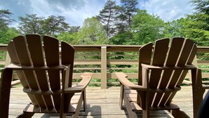 Two wooden Adirondack chairs on a wooden deck with a view of trees and a cloudy sky. - Fireside Lodge - Hosted by The Chalets (Logan)