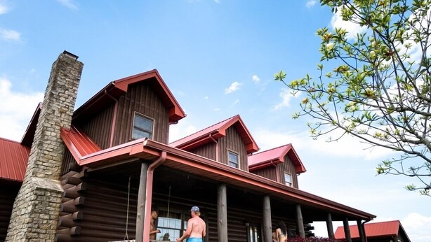 A log cabin with a stone chimney, a porch with railings, and a well-maintained garden. - Big Sky Lodge - Hosted by The Chalets (Logan)