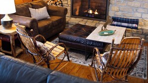 A cozy living room with a stone fireplace, wooden furniture, and a framed picture on the wall. - Big Sky Lodge - Hosted by The Chalets (Logan)
