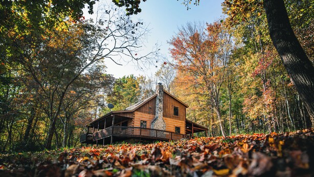 A cabin with a stone chimney, surrounded by autumn foliage.