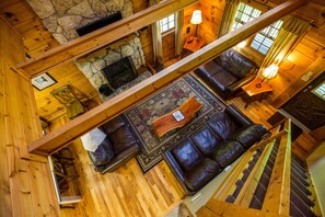Cozy cabin with a high ceiling, exposed beams, and a stone fireplace, featuring a comfortable living area with a sofa set and area rug.