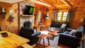 A cozy log cabin interior with a stone fireplace, wooden furniture, and a television mounted on the wall.