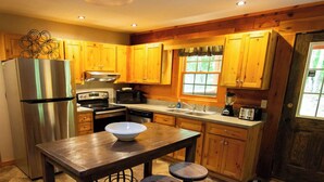 A kitchen with wooden cabinets, a stainless steel refrigerator, a stove, and a sink. There is a wooden table with stools.