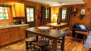 A cozy cabin-style kitchen with wooden cabinets, a central island with stools, a dining table, and a sofa in the living area.