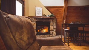 A cozy living room with a stone fireplace, leather armchair, and wooden dining table. - A-Frame #07 - Hosted by The Chalets (Logan)
