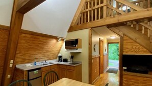 A rustic kitchen with wooden beams, a dining table, chairs, and a microwave. - A-Frame #07 - Hosted by The Chalets (Logan)