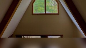 A room with a sloped ceiling and a window with a wooden frame. - A-Frame #03 - Hosted by The Chalets (Logan)