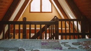 Une chambre mansardée avec un plafond en pente, des poutres en bois et une fenêtre.