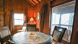 Un intérieur en bois avec une table ronde et quatre chaises, une fenêtre avec des rideaux et une lampe.