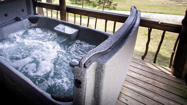 Un bain à remous sur une terrasse en bois, avec vue sur un champ verdoyant et des arbres.