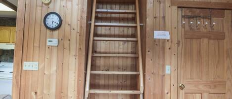 Un interior de madera con una escalera, un sofá, una puerta y un reloj de pared.
